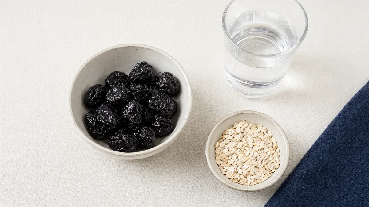Bowls of prunes and oats beside a water glass.