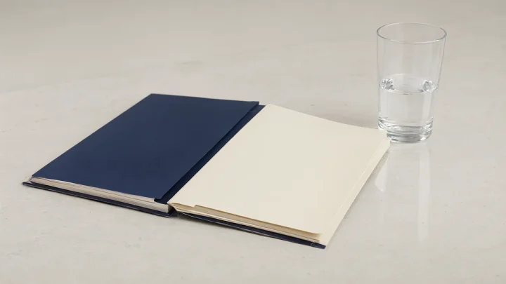Two closed folders beside a glass of water.