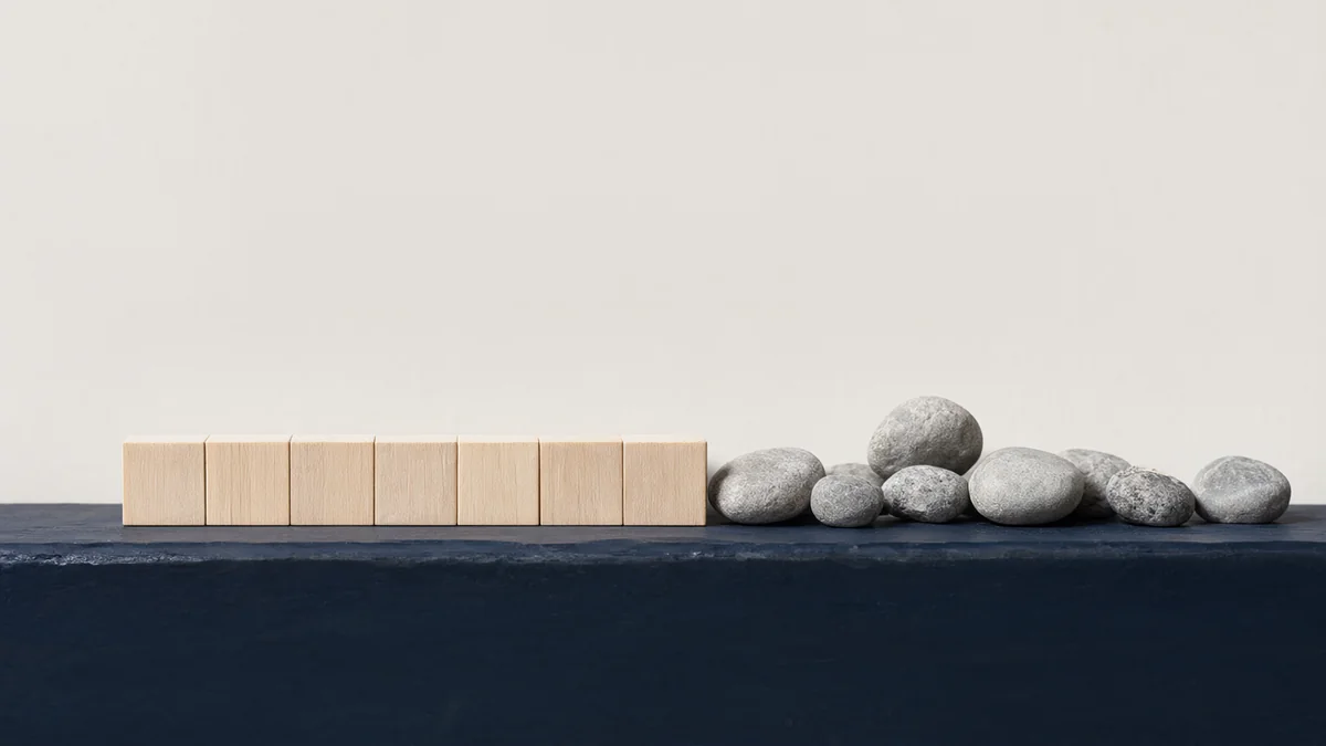 Uniform wooden blocks beside a varied group of natural pebbles.