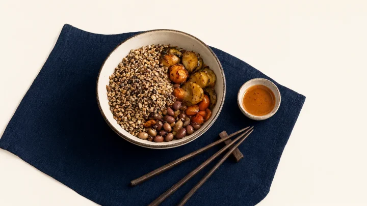 A mixed grain bowl with vegetables, beans and a sauce dish.