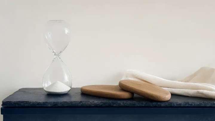A sand hourglass beside two smooth wooden oval shapes.