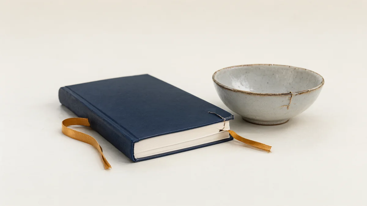 A closed notebook beside a repaired ceramic bowl.